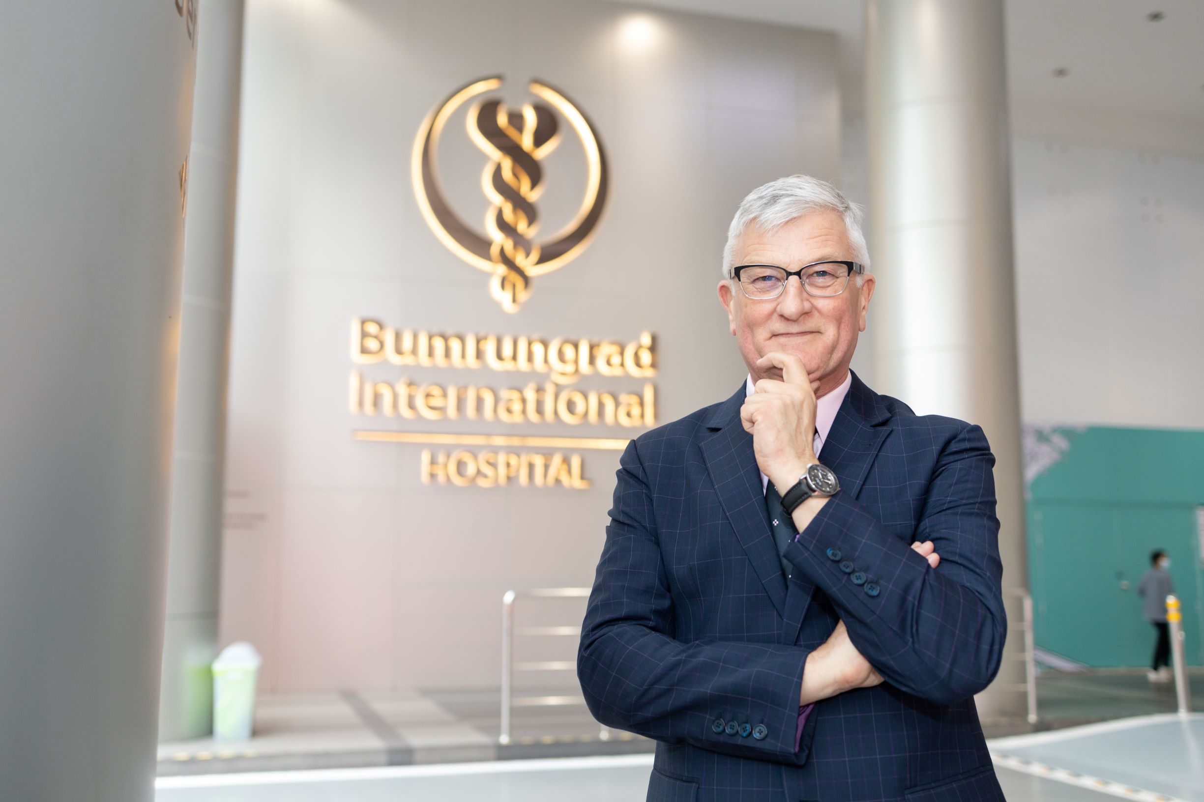 Jeremy Ford Profile, standing in front of Bumrungrad International Hospital logo